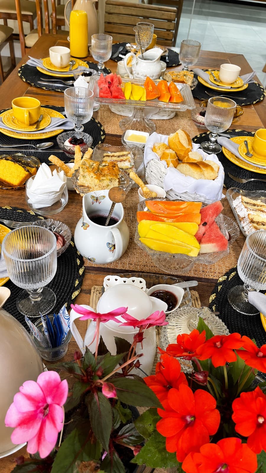 Mesa do café da manhã com arranjo de flores vermelhas e frutas cortadas