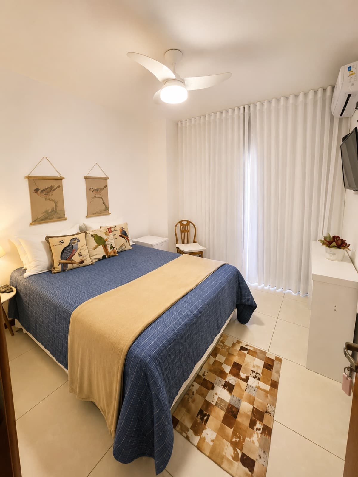 Quarto com cama de casal, roupa de cama azul e tapete de couro