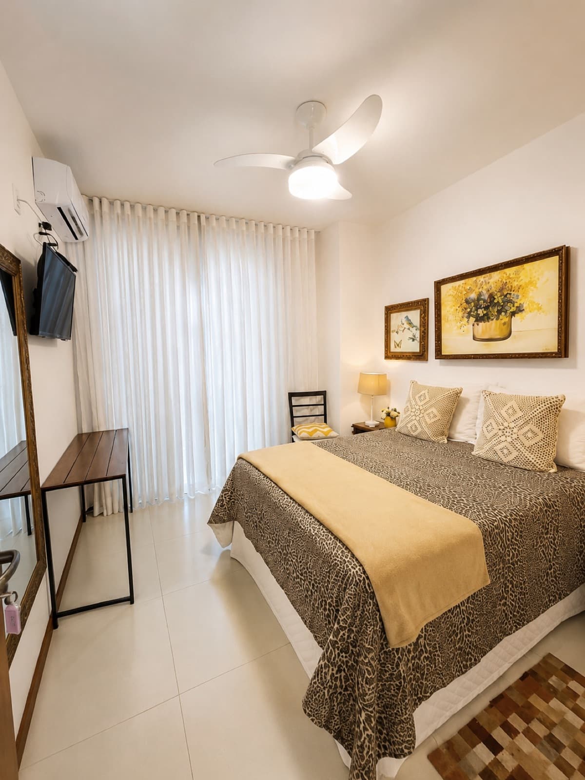 Quarto com cama de casal, colcha bege e quadro de flores na parede