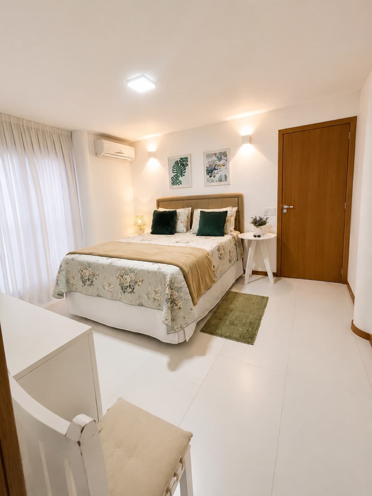 Quarto claro com cama de casal, colcha floral e cortinas até o chão