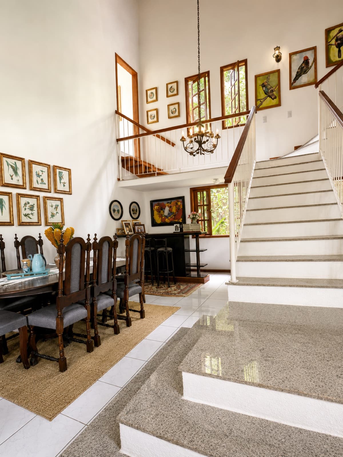 Sala de jantar com mesa de madeira e parede de quadros até o pé-direito alto